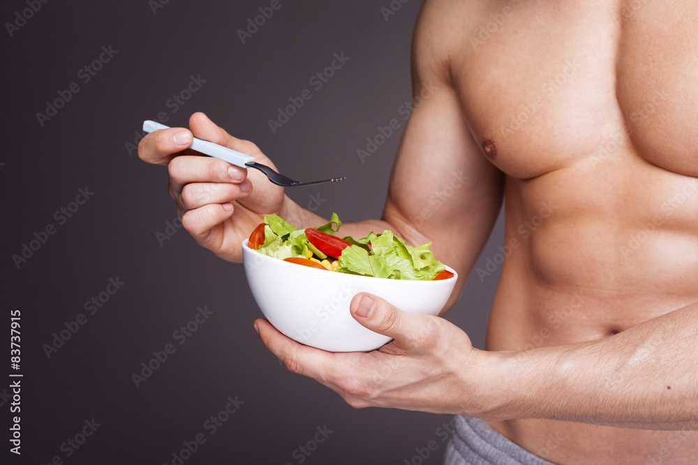 Fit man holding a bowl of fresh salad on grey background Fit man holding a bowl of fresh salad on grey background