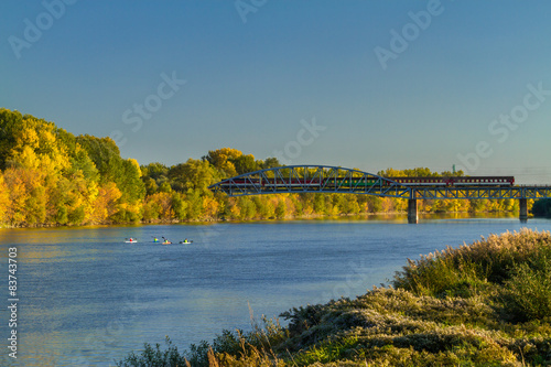 Autumn at river with kayaks and train crossing bridge.