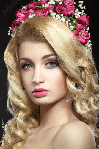 Portrait of a beautiful blond girl with a wreath of purple flowers on her head. Photo shot in the Studio on a grey background