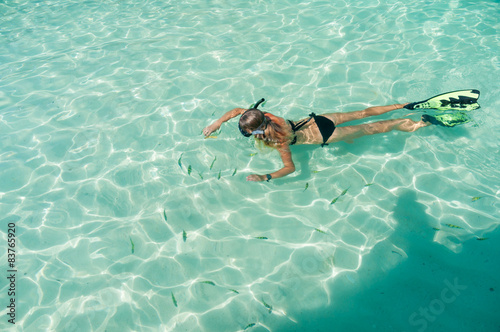 Girl snorkeling in a shallow water with fish