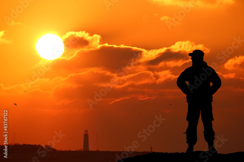 Silhouette shot of soldier holding gun with colorful sky 