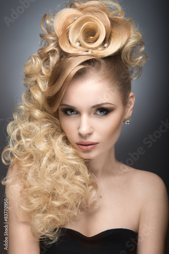 Beautiful blonde girl in evening dress with an unusual hairstyle in the form of roses and bright makeup. Beauty face. Picture taken in the studio on a gray background.