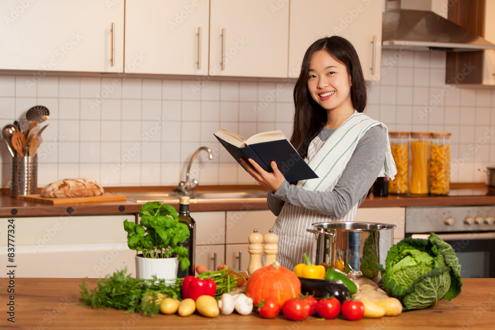 Asian smiling woman looking a cookbook