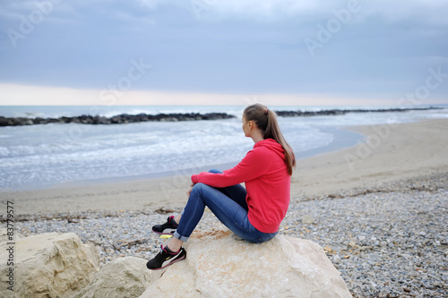 The girl sits alone ashore among stones