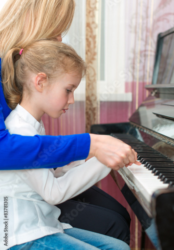 Woman teaching little girl to play the piano.