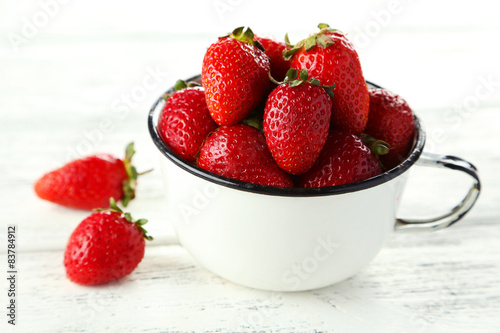 Strawberries in cup on white wooden background