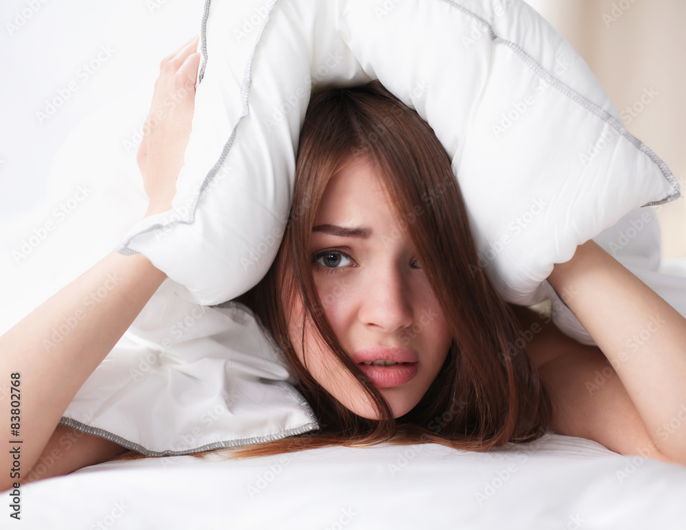 Female lying on bed and closing her ears with pillow Female lying on bed and closing her ears with pillow