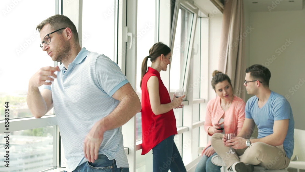 Sad man looking out the window while his friends chatting
Sad man looking out the window while his friends chatting