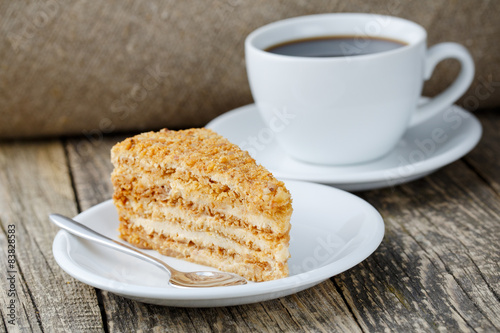 Tasty honey cake with cup of coffee on wooden background.