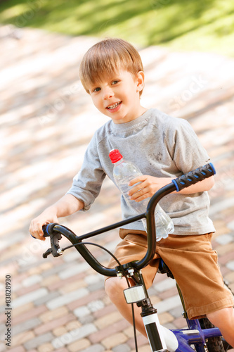 Smiling boy riding bike with bottle of water
