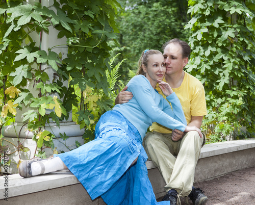 Fotografie, Tablou Young happy couple sits in the arbour twined greens