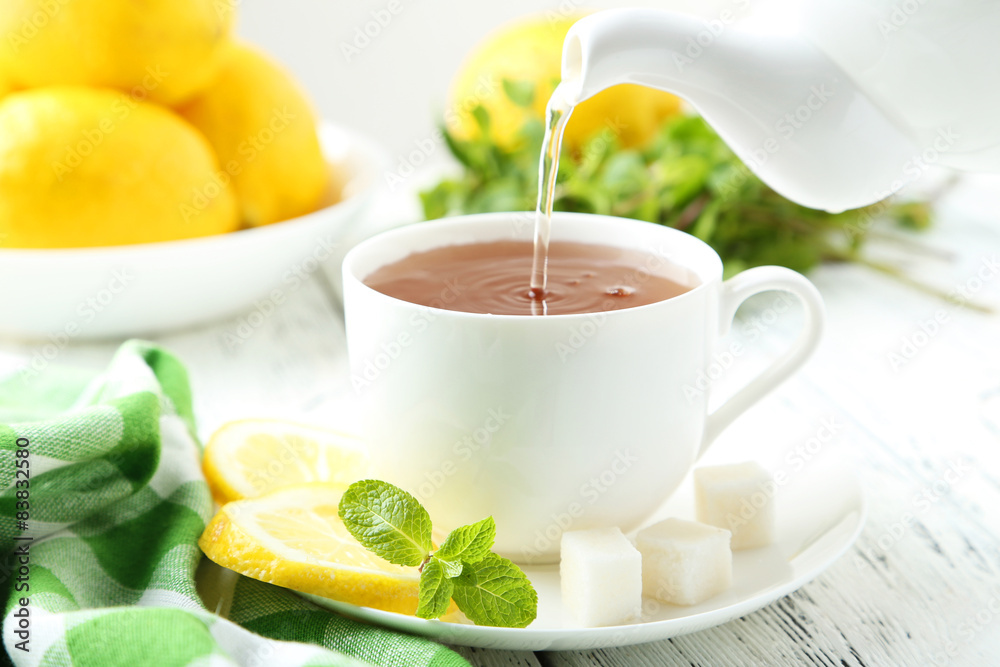 Pouring tea into cup of tea on white wooden background Pouring tea into cup of tea on white wooden background