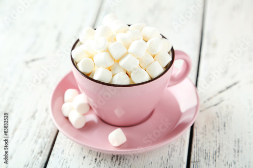 Marshmallows in pink cup on white wooden background