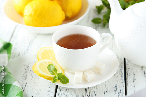 Cup of tea with mint and lemon on white wooden background