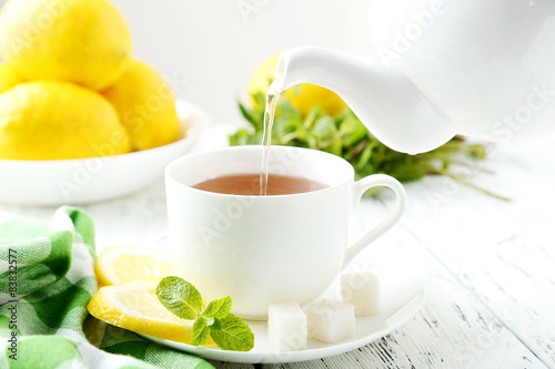 Fototapeta Naklejka Na Ścianę i Meble -  Pouring tea into cup of tea on white wooden background