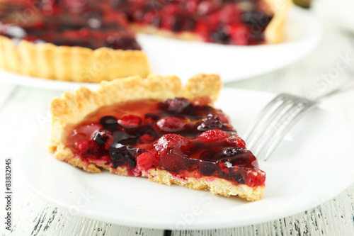 Fresh berry tart on plate on white wooden background