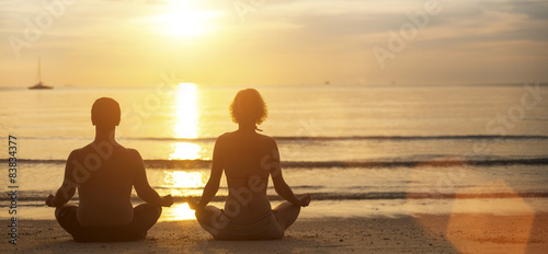 Man and woman yoga silhouettes meditating on Sea coast.