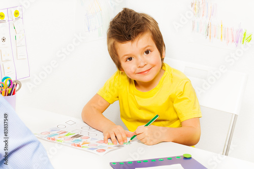 Smiling small boy coloring the shapes on paper