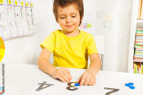 Smiling boy put coins on numbers learning count
