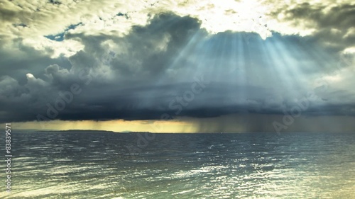 Squally wind and beams of sunlight shoot through storm clouds.
 photo