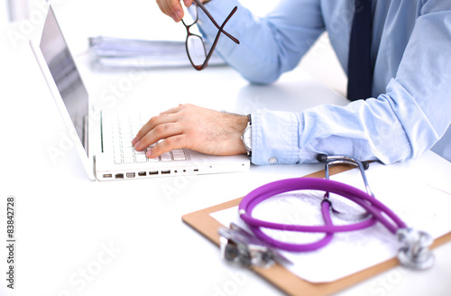 Male doctor using a laptop, sitting at his desk  photo