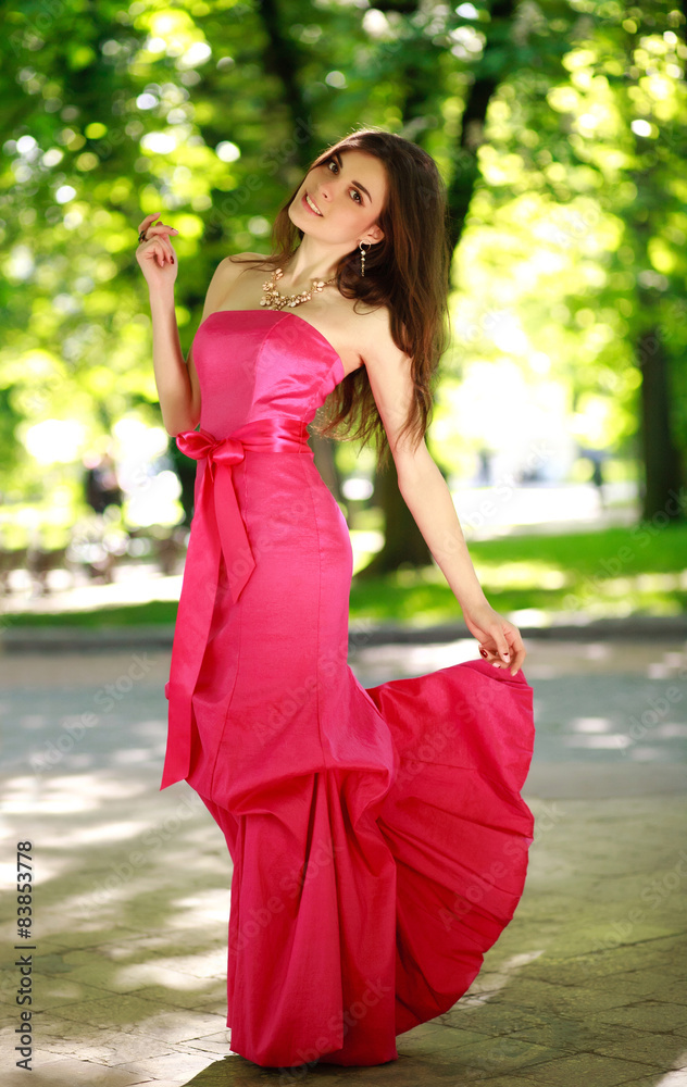 Happy young woman in a luxury long dress in a summer park