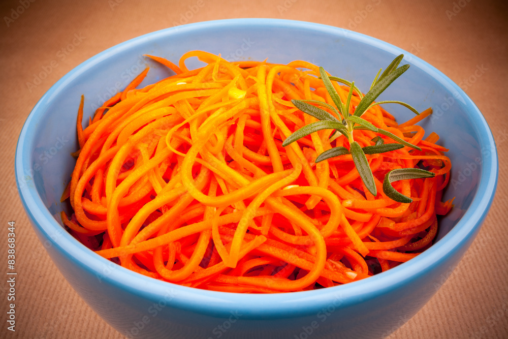 Spicy carrot salad in blue bowl on brown background Spicy carrot salad in blue bowl on brown background
