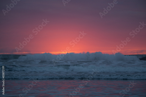 Pacific ocean bright orange and red sunset behind ocean waves.