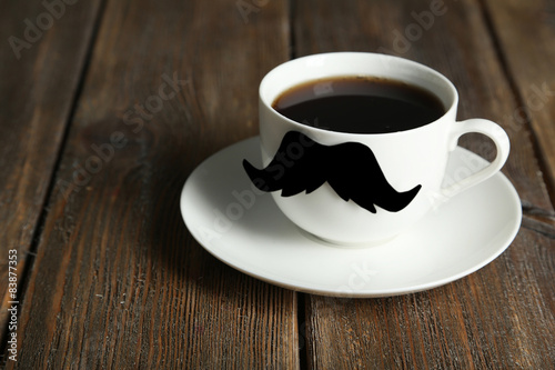 White cup with paper mustache on brown wooden background