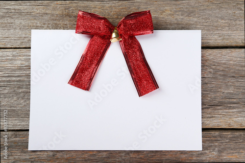 Blank paper sheet with red bow on grey wooden background