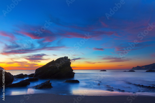 Long exposure milky ocean and cliff with small stones at sunset