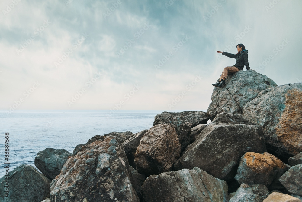Woman sitting on stone coast Woman sitting on stone coast