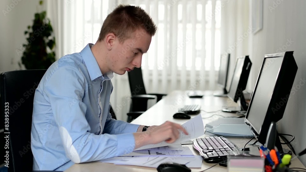 young handsome man works on desktop computer and reads document in the office young handsome man works on desktop computer and reads document in the office