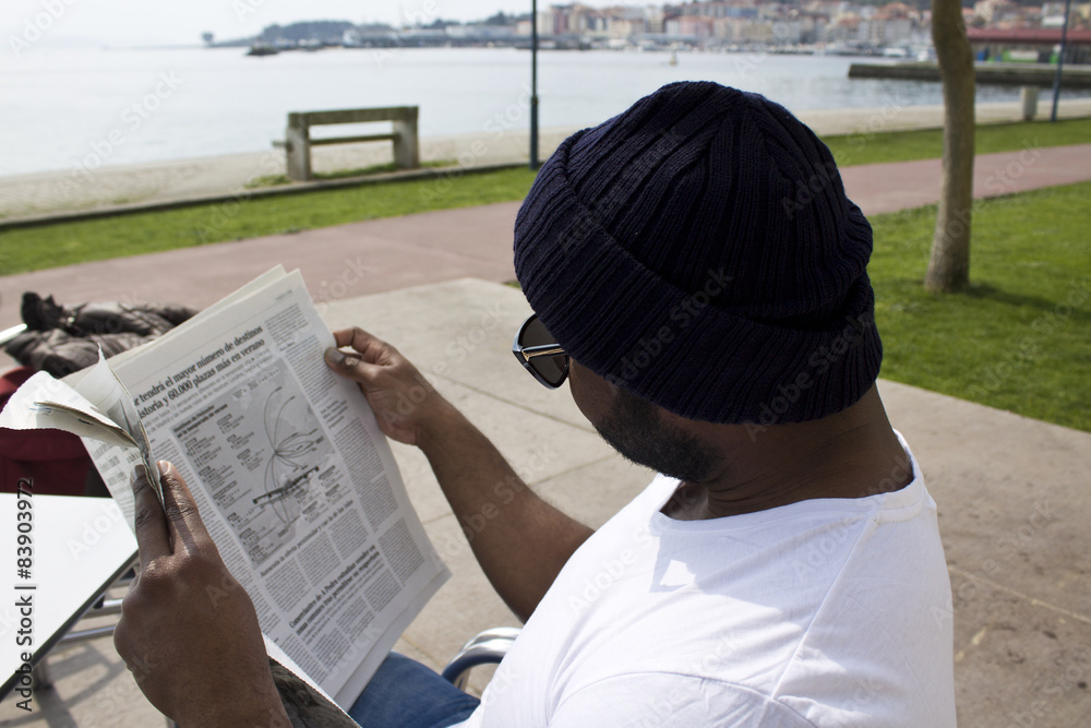 Naklejka premium black man reading newspaper on the terrace