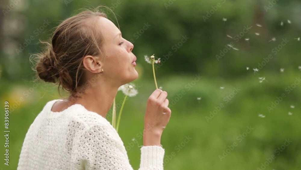 Beautiful woman blowing a dandelion on a meadow on a lovely sunny day Beautiful woman blowing a dandelion on a meadow on a lovely sunny day