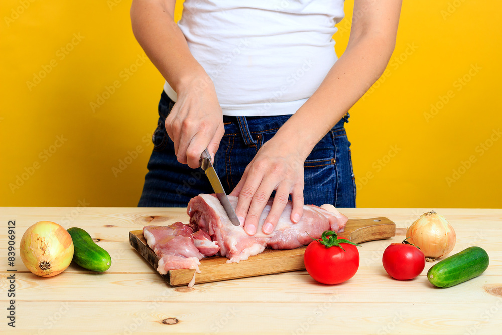 Woman in the kitchen is cutting pork on cutting board
