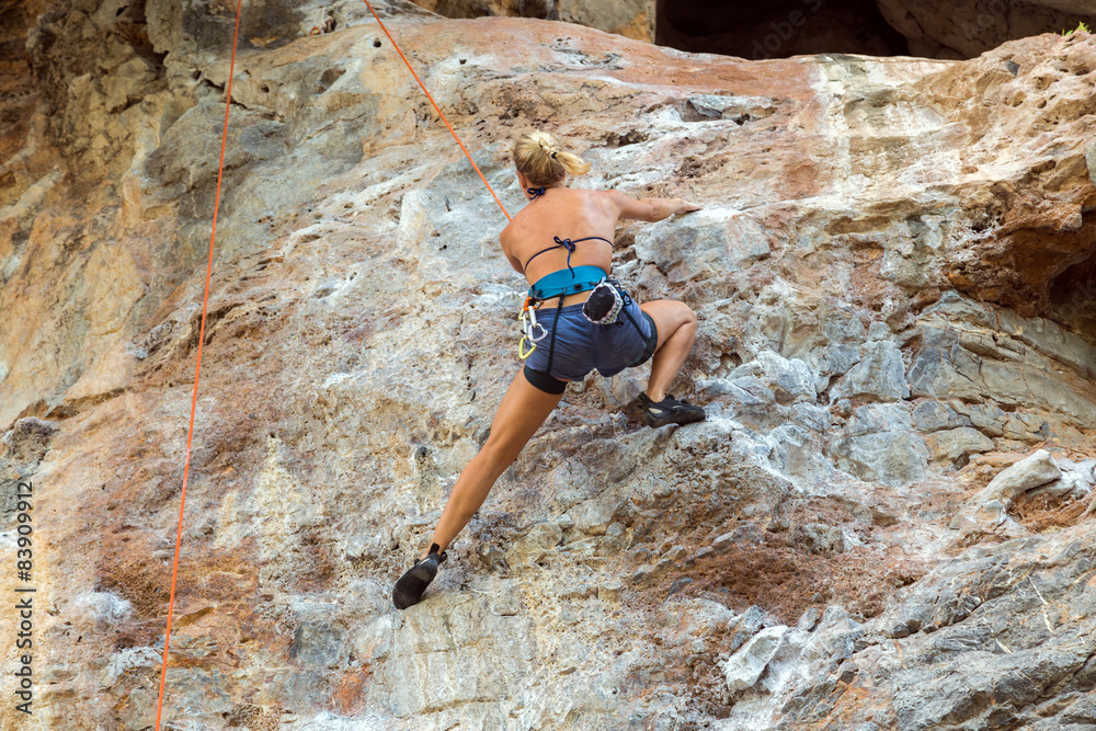 Female rock climber clinging to a cliff