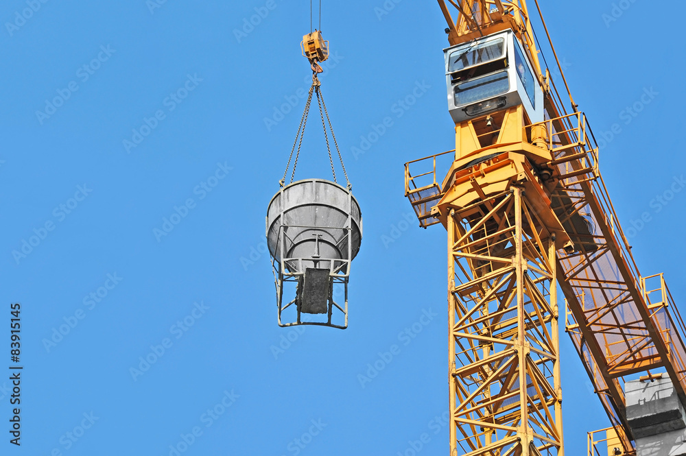 Fototapeta premium Crane lifting concrete mixer container against blue sky