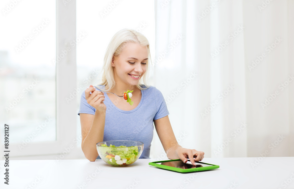 smiling woman eating salad with tablet pc at home