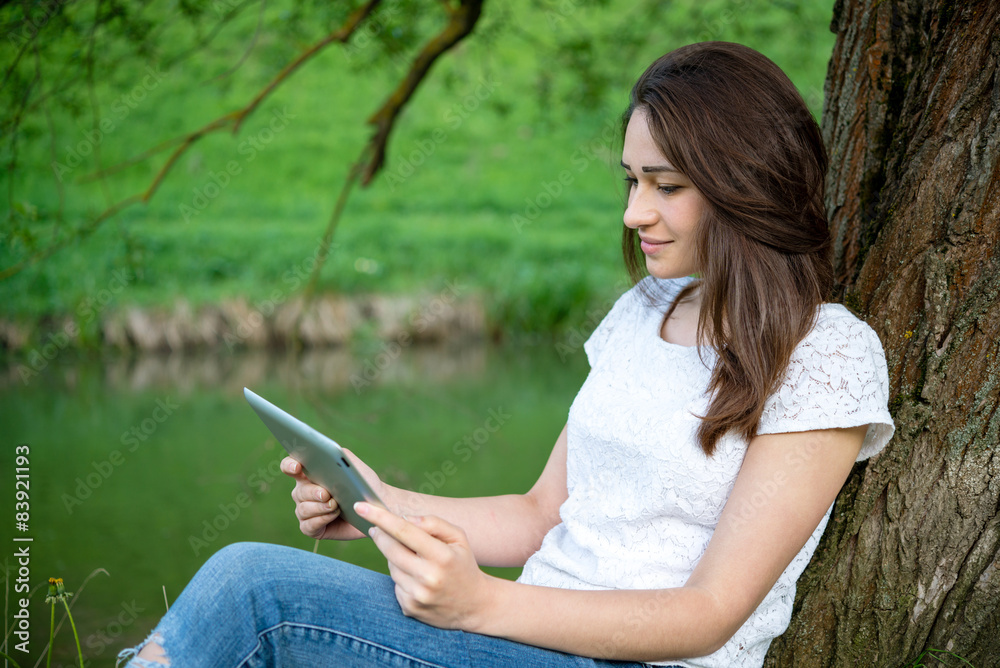 girl holding the tablet while sitting under a tree girl holding the tablet while sitting under a tree