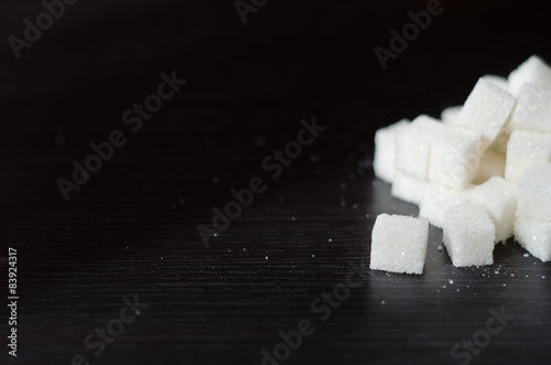 White sugar cubes piled in heap on the black desk