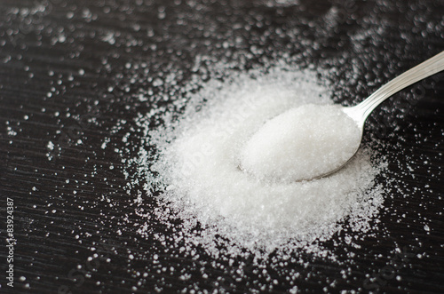 white sugar scattered on a metal spoon black table