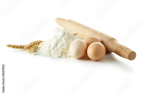 Heap of wheat flour with eggs, rolling pin and spikelets isolate photo