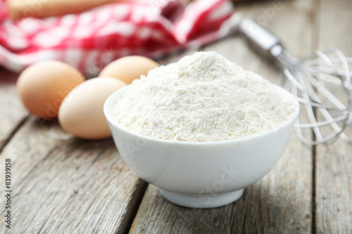 Bowl of wheat flour with eggs and whisk 