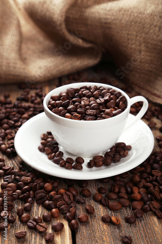 Cup full of coffee beans on brown wooden background