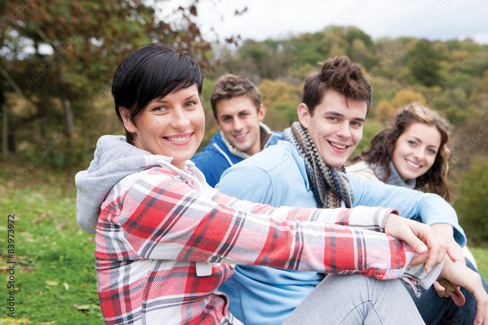 Four friends sit together outdoors and smile for the camera Four friends sit together outdoors and smile for the camera