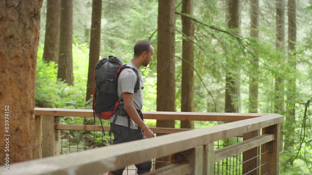 A man in a backpack looks over a deck to see the forest trail he has hiked A man in a backpack looks over a deck to see the forest trail he has hiked