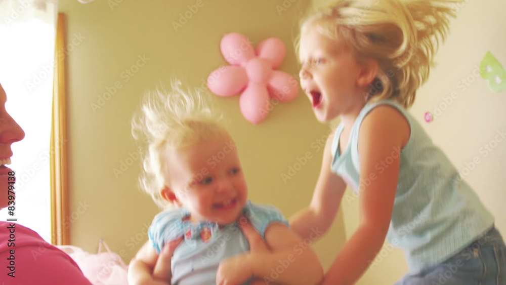 A young girl jumps on her bed as her mother and sister play next to her