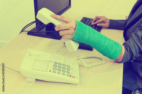 Injured businesswoman with green cast on the wrist holding telep photo