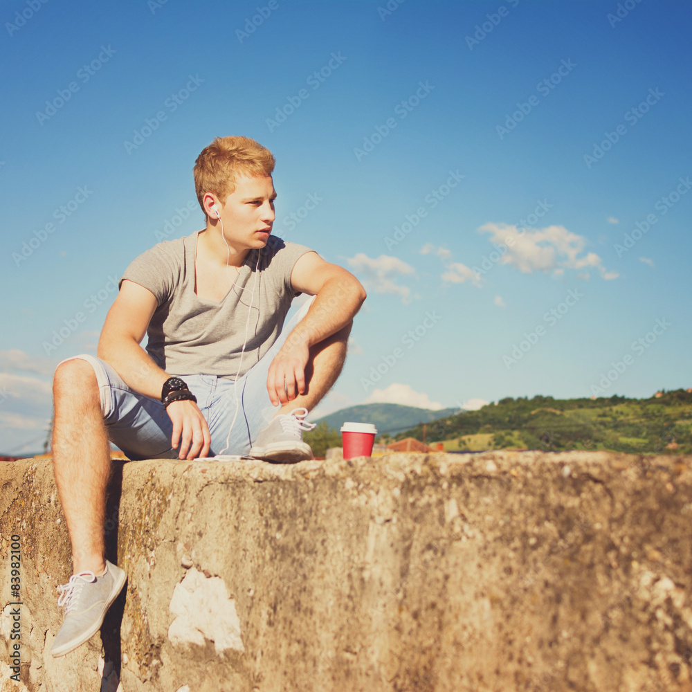 Young man with takeaway coffee relaxing outdoors in summer 
